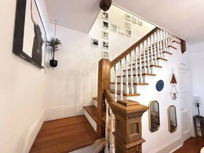 Eine Treppe mit einem hölzernen Geländer und weißen Spindeln, einer Kübelpflanze sowie gerahmten Bildern an der Wand.