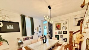 Un comedor con una larga mesa, sillas, una araña y una escalera.