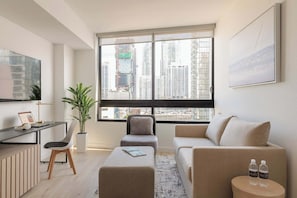 A modern living room with a large window, a sofa, a coffee table, a desk with a laptop, and a plant. - City Dreams Sauna, Rooftop Pool & Parking (Miami)