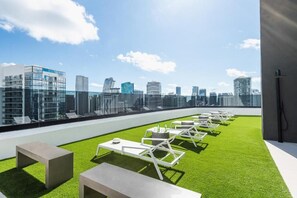A rooftop terrace with artificial grass, white lounge chairs, and tables, offering a city skyline view. - City Dreams Sauna, Rooftop Pool & Parking (Miami)