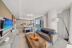 Una sala de estar moderna con sofá, mesa de centro, televisor y una cocina al fondo.