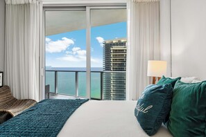 A hotel room with a large bed, a view of the ocean, a balcony, and a high-rise building in the background. - Sea Glass  Pool, Gym, Oceanfront in Hollywood FL (Hollywood)