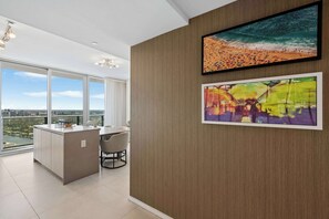 A modern interior with a dining area, a kitchen island, and a large window offering a city view. - Sea Glass  Pool, Gym, Oceanfront in Hollywood FL (Hollywood)