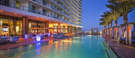 A multi-story hotel with a swimming pool, outdoor seating, and palm trees.
