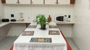 Cozinha com armários brancos, micro-ondas, mesa com toalha branca e um banco.
