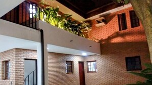 Um edifício com vários níveis, paredes de tijolo, uma escadaria e um pequeno pátio com grama e plantas.