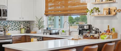 Une cuisine moderne dotée d’un îlot central, d’appareils électroménagers en acier inoxydable et d’une fenêtre avec des stores.