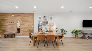 A modern dining area with a wooden table and chairs, a mounted TV, and framed artwork on the wall. - Elegant 3BR Retreat  close to Hospital & Downtown (East Ridge)