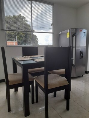 A dining area with a table and chairs, a refrigerator, and a window with blinds. - Very Affordable Apartment Just 3' from Parque del Café (Montenegro Province)
