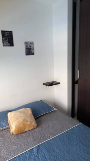 A bedroom with a bed, pillows, a small shelf, and a door. - Very Affordable Apartment Just 3' from Parque del Café (Montenegro Province)