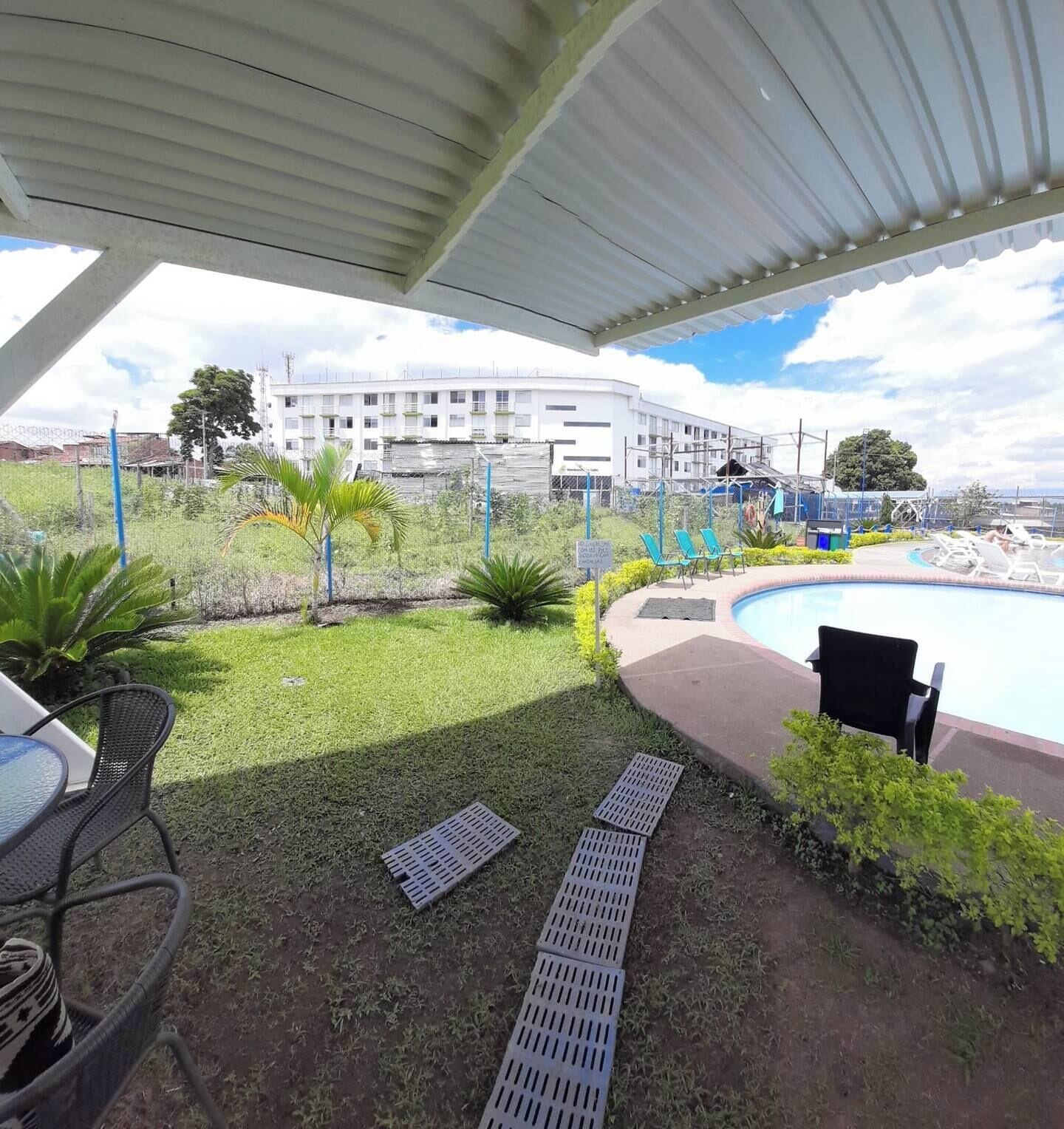 Ein überdachter Außenbereich mit Pool, Liegestühlen und einem Gebäude im Hintergrund.