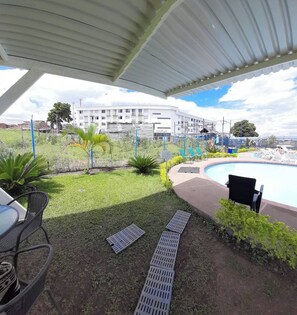 A covered outdoor area with a pool, lounge chairs, and a building in the background. - Very Affordable Apartment Just 3' from Parque del Café (Montenegro Province)