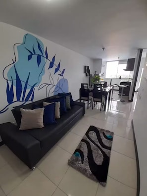 A modern living room with a black sofa, a coffee table, and a large abstract wall mural. - Very Affordable Apartment Just 3' from Parque del Café (Montenegro Province)
