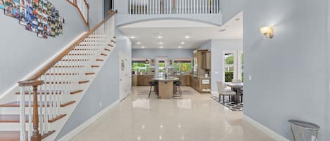 A spacious interior with a central island, a staircase with white railings, and a balcony with railings.