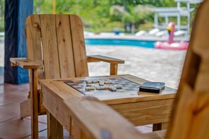 Una sedia e un tavolo di legno con una scacchiera e domino, vicino a una piscina con un gonfiabile a forma di fenicottero.