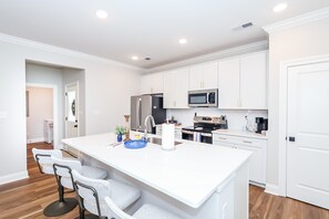 A modern kitchen with white cabinetry, stainless steel appliances, and a central island with bar stools. - The Grove Getaway at Patterson Place (Oxford)