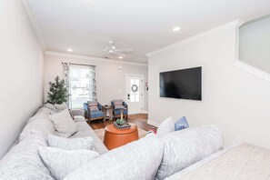 A living room with a sectional sofa, a coffee table, and a TV mounted on the wall. - The Grove Getaway at Patterson Place (Oxford)