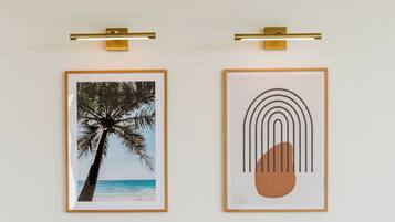 Une chambre d’hôtel bien aménagée, avec une tête de lit en bois, une lampe de chevet, un tableau représentant un palmier et une œuvre d’art abstraite encadrée.