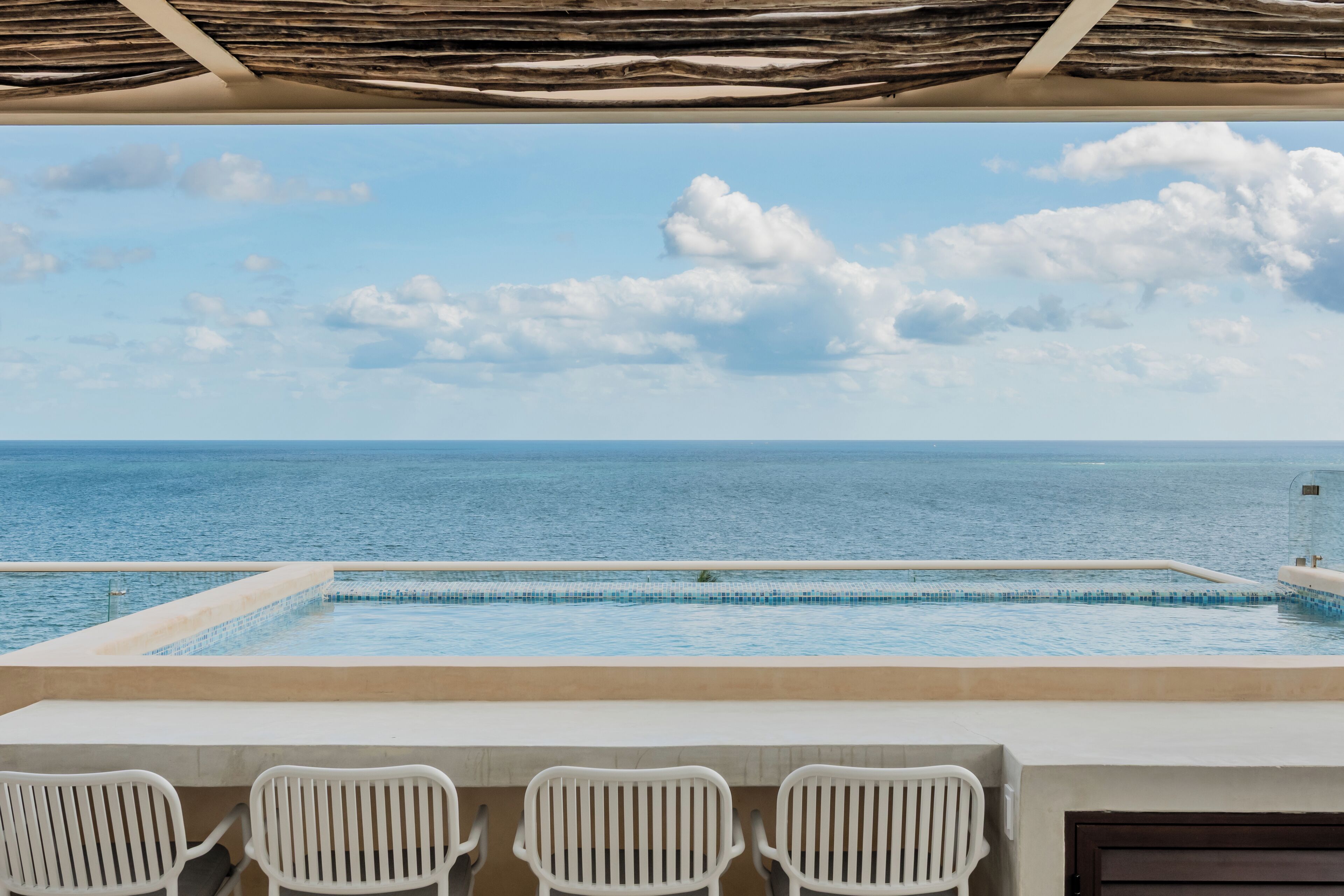 Ein Pool mit Blick auf das Meer, weiße Stühle und eine Holzdecke.