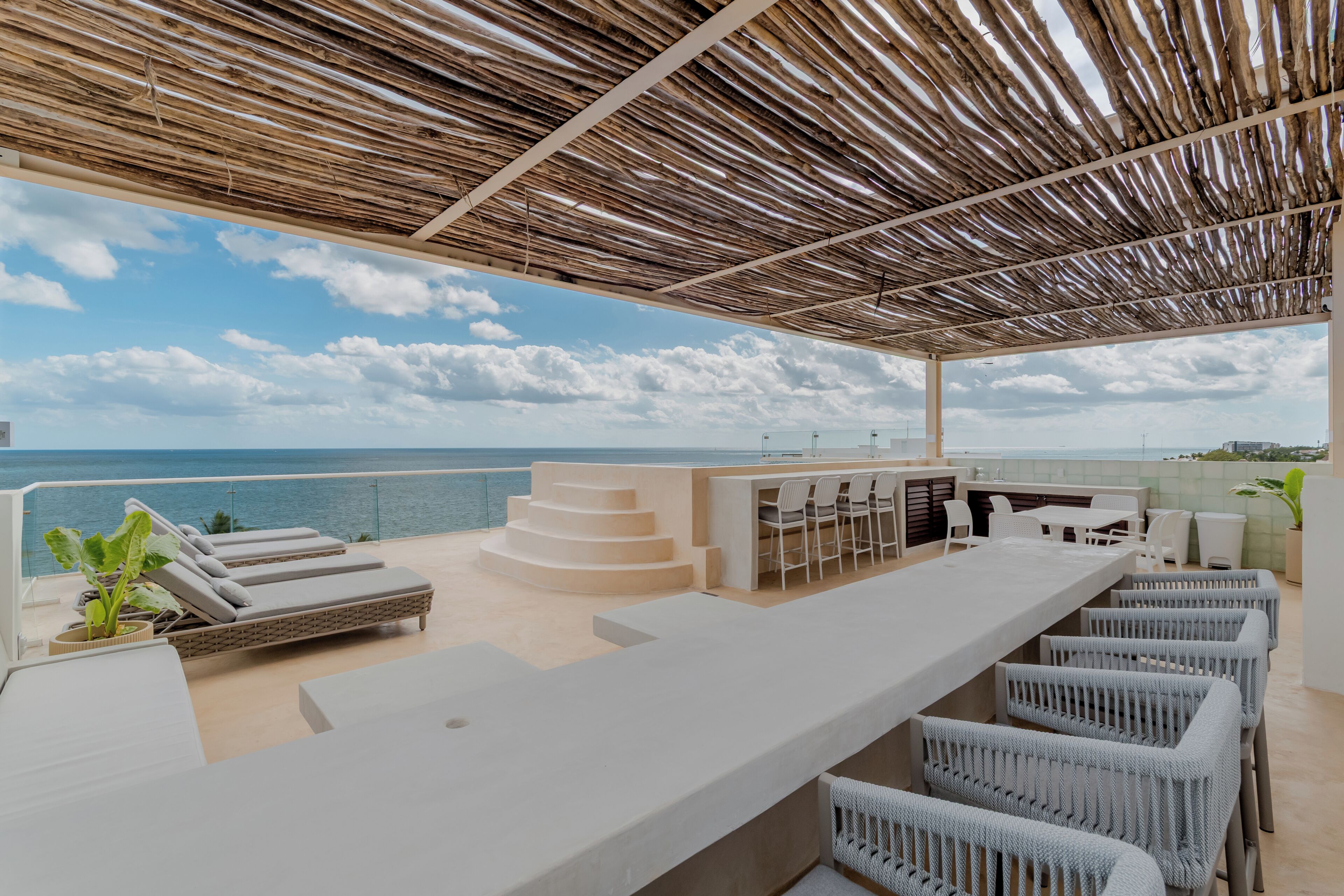 Un bar situé sur le toit, offrant une vue sur la mer, avec des places assises en plein air et une structure en forme de pergola.