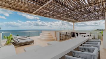 Un bar situé sur le toit, offrant une vue sur la mer, avec des places assises en plein air et une structure en forme de pergola.