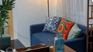 Ein Wohnzimmer mit einem blauen Sofa, einem Bild an der Wand, einer Lampe und einem Tisch mit einer Pflanze.