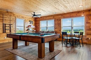 Ein Holzinterieur mit Billardtisch, Sesseln und Deckenventilator.