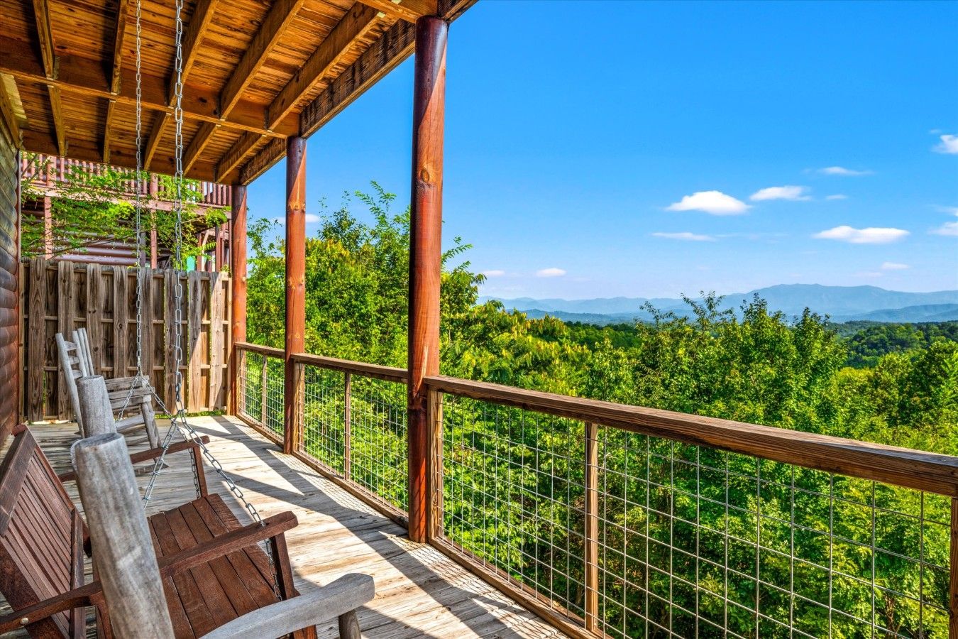 A wooden deck with chairs and a swing overlooking a forested landscape.