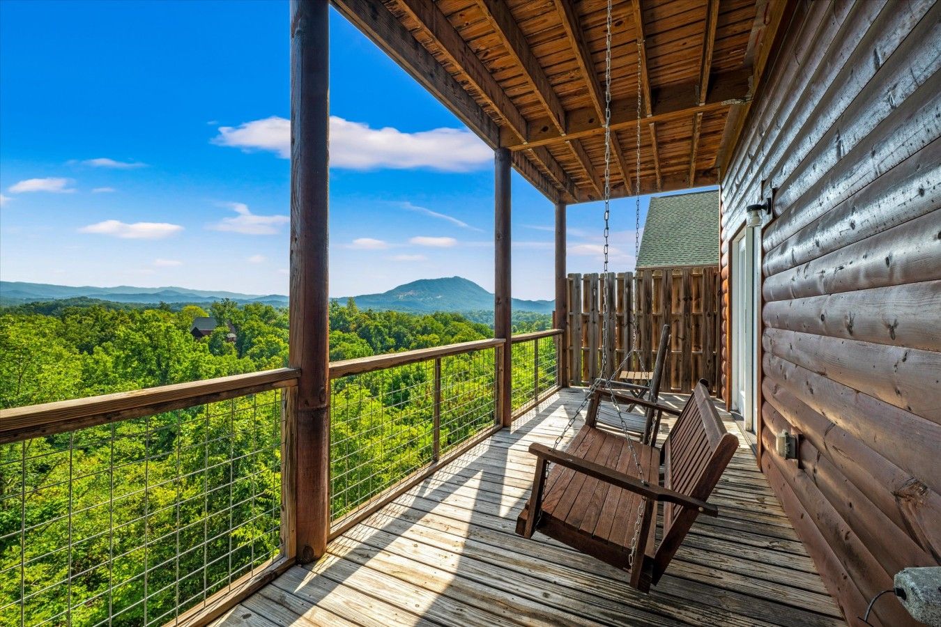 A wooden deck with a swing chair, a view of a forest, and a mountain in the distance.