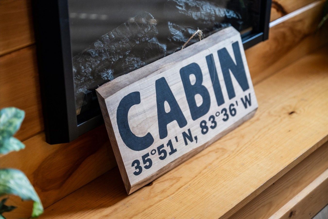 Un panneau en bois portant l’inscription « CABIN » et les coordonnées « 35°51’N, 83°36’O » sur une surface en bois.