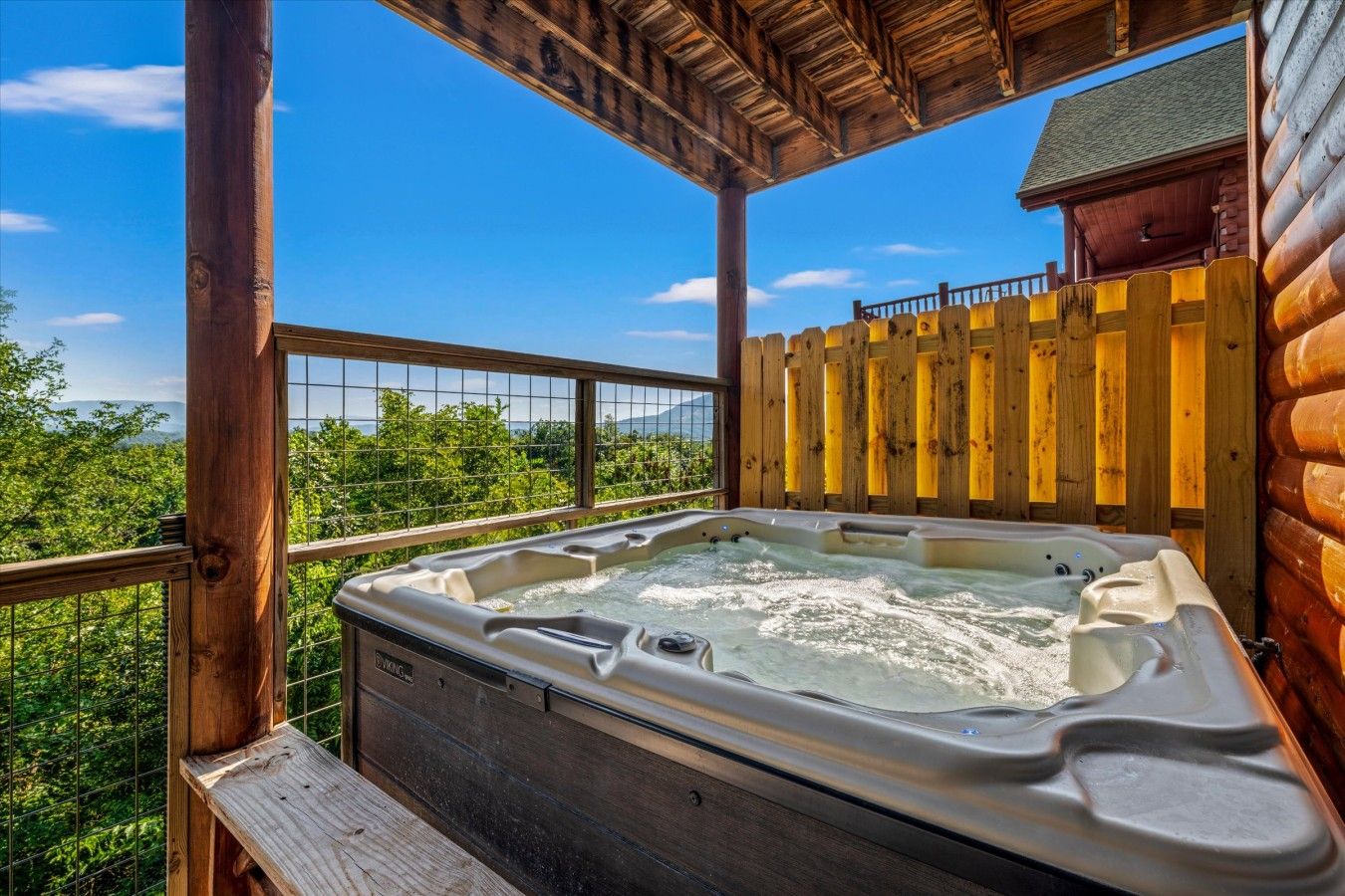 Un bain à remous sur une terrasse en bois, avec vue sur les arbres et les montagnes.