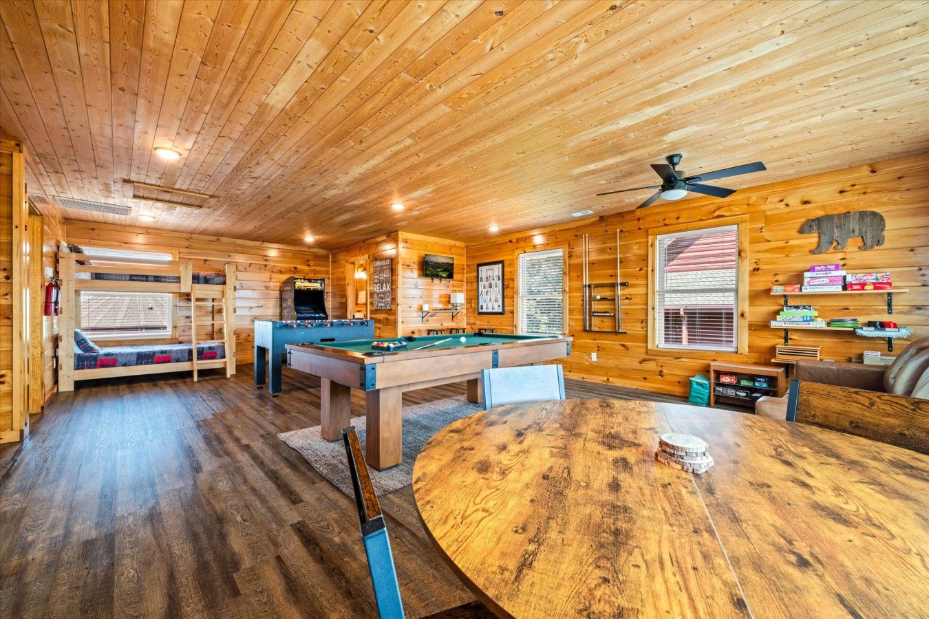 A wooden cabin interior with a pool table, a foosball table, and a billiards table.