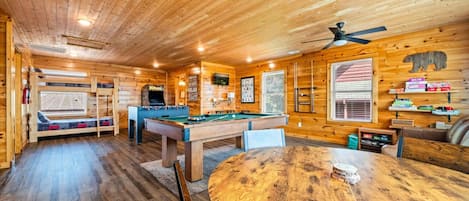 A wooden cabin interior with a pool table, a foosball table, and a billiards table.