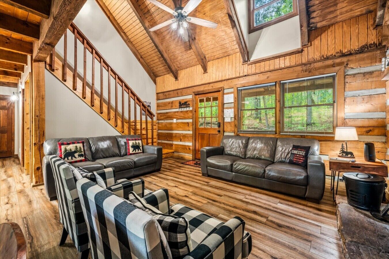 A log cabin interior with a staircase, leather sofas, and a fireplace.
