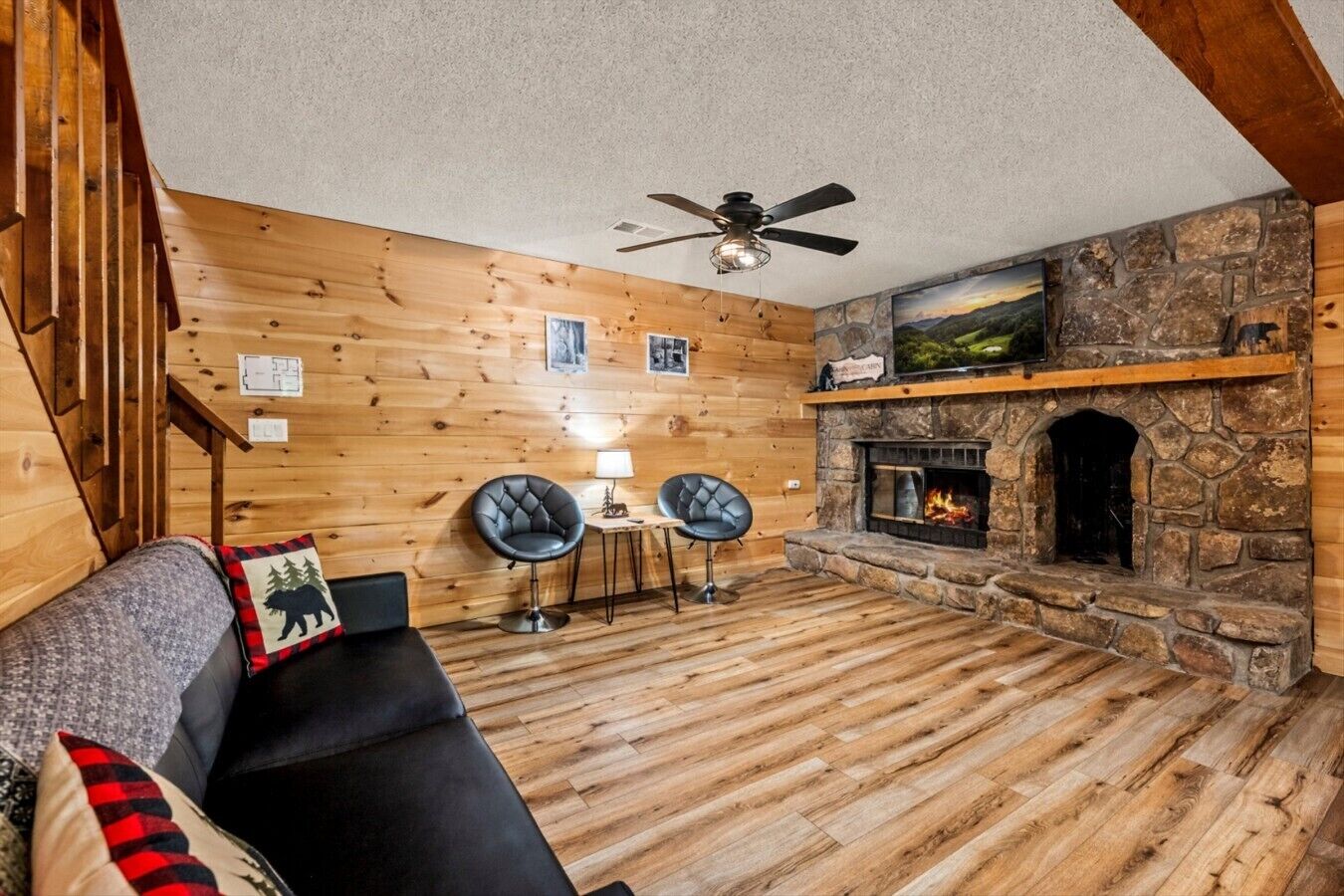 Ein gemütliches Blockhaus-Interieur mit Kamin aus Stein, Holzwänden, Deckenventilator und einem schwarzen Ledersofa.