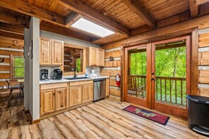 Cocina tipo cabaña con armarios de madera, lavavajillas de acero inoxidable y un ventanal con vistas a un bosque.