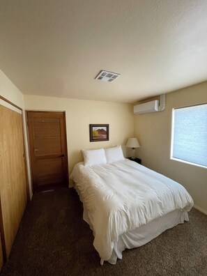 A bedroom with a bed, a door, a wall-mounted air conditioner, a window, and a painting. - Mountain Chalet next to Angeles National Forrest and near Hard Rock Casino Tejon (Frazier Park)