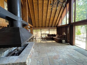 A spacious living area with a stone floor, a large fireplace, wooden beams, and a view through large windows. - Mountain Chalet next to Angeles National Forrest and near Hard Rock Casino Tejon (Frazier Park)