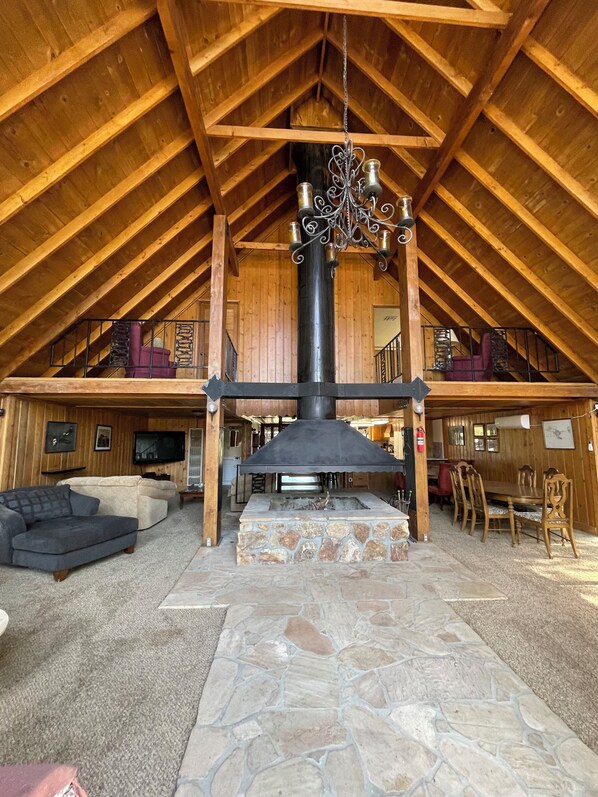 A spacious loft with a high ceiling, a stone fireplace, and a dining area with wooden furniture.