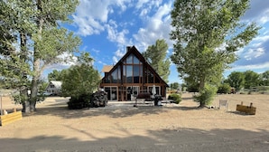 A rustic cabin with a large window, a barbecue area, and a dirt driveway. - Mountain Chalet next to Angeles National Forrest and near Hard Rock Casino Tejon (Frazier Park)
