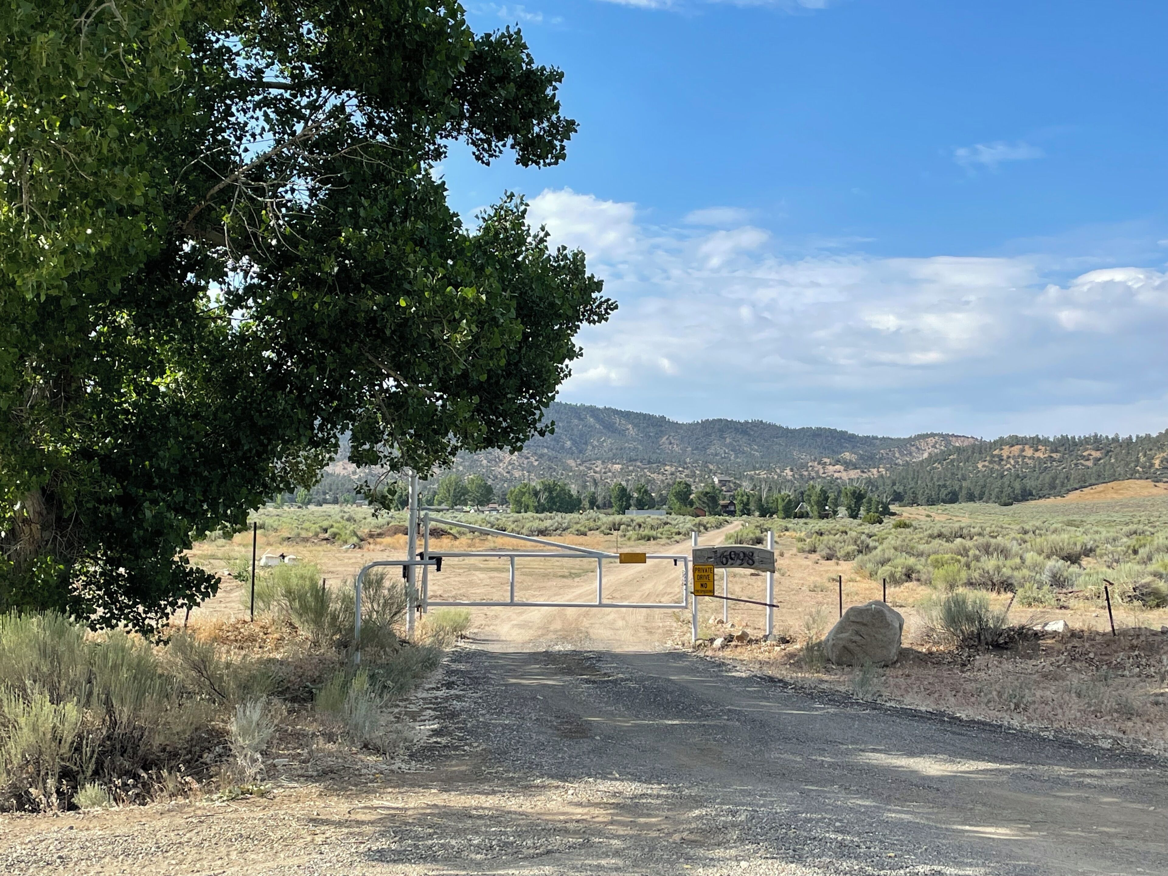 Ein verschlossenes Tor zu einem Privatgrundstück, eine unbefestigte Straße führt durch eine hügelige Landschaft.