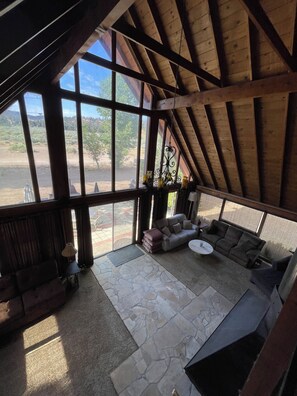A spacious room with a high ceiling and large windows, a stone floor, and a cozy seating area with a sofa and a coffee table.