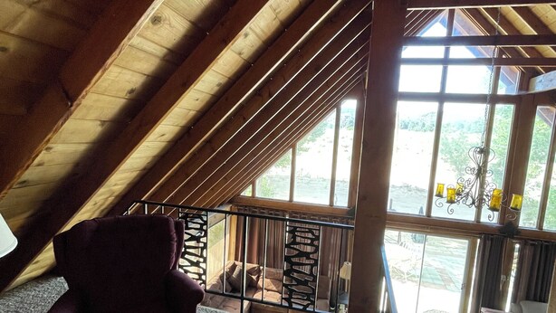 An attic room with a sloped ceiling, a purple chair, a view through a window, and a staircase leading to an upper level. - Mountain Chalet next to Angeles National Forrest and near Hard Rock Casino Tejon (Frazier Park)