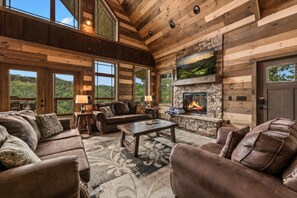 A spacious living room with a fireplace, leather sofas, and large windows offering a view of the outdoors. - 5BR w/Indoor Pool*Theater*Game Room*Hot Tub*Views (Pigeon Forge)