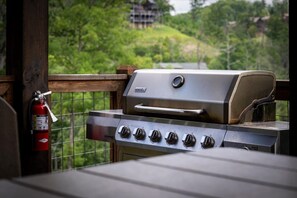 A barbecue grill with multiple burners and a digital display, positioned on a balcony with a view of greenery and a distant building. - 5BR w/Indoor Pool*Theater*Game Room*Hot Tub*Views (Pigeon Forge)