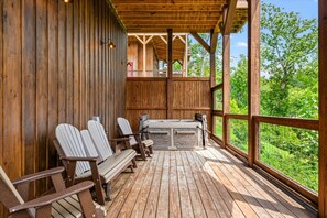 A wooden deck with Adirondack chairs and a hot tub, overlooking a lush green landscape. - 5BR w/Indoor Pool*Theater*Game Room*Hot Tub*Views (Pigeon Forge)