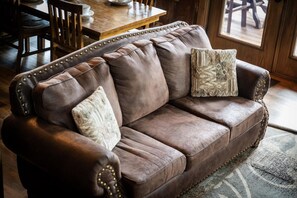 A brown leather sofa with gold studs, two pillows, and a wooden table in a room with a patterned rug. - 5BR w/Indoor Pool*Theater*Game Room*Hot Tub*Views (Pigeon Forge)