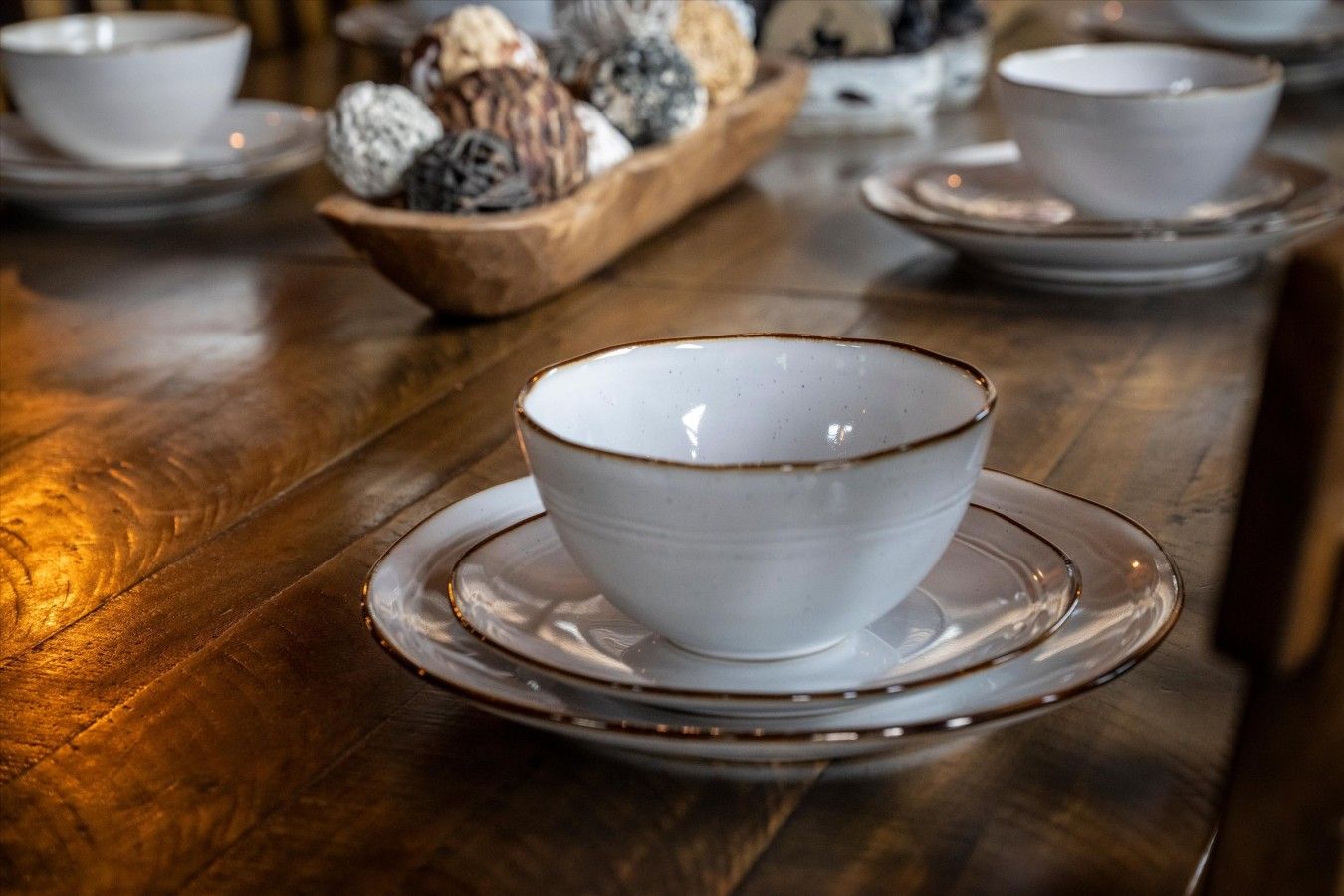 Ein Holztisch mit einer weißen Schüssel und einem Untertasse im Vordergrund, sowie eine weitere Holztisch mit Dekoration im Hintergrund.
