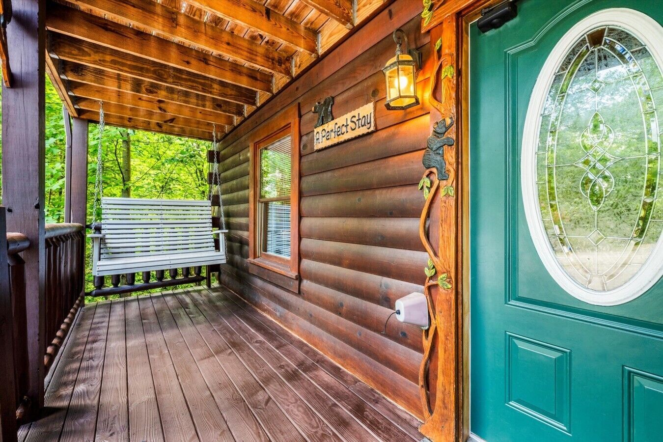 Eine Holzhütte mit Veranda, einer Bank, einem Schild mit der Aufschrift 'A Perfect Stay' und einer grünen Tür mit Fenster.