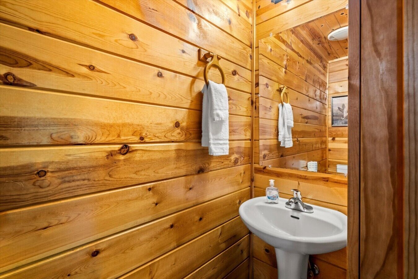 Een betegelde badkamer met een wastafel, handzeep en een handdoek aan een rek.